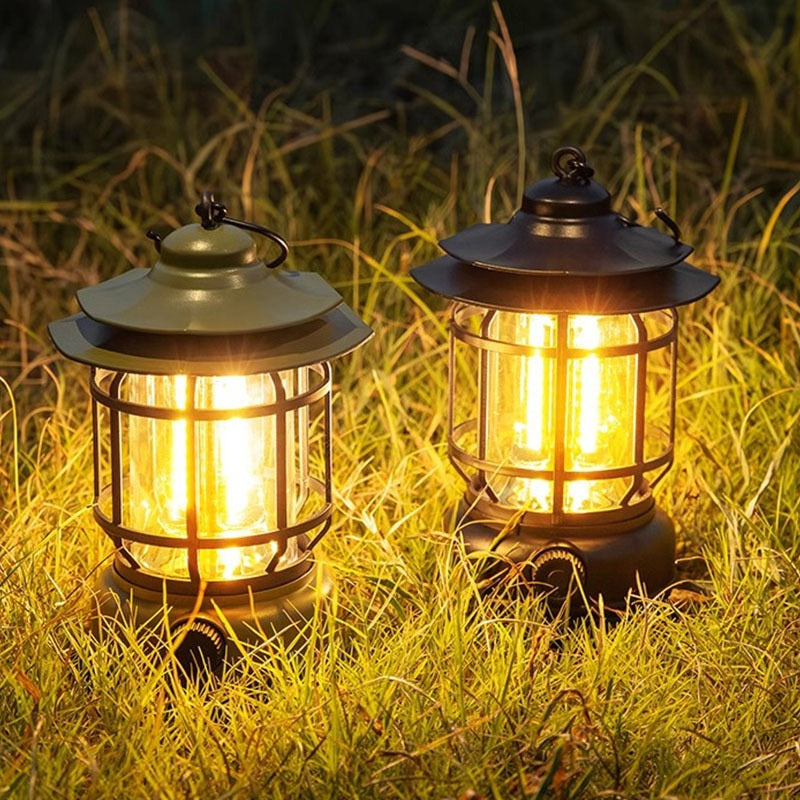 Two retro camp lanterns lit in long grass at night, olive green and black