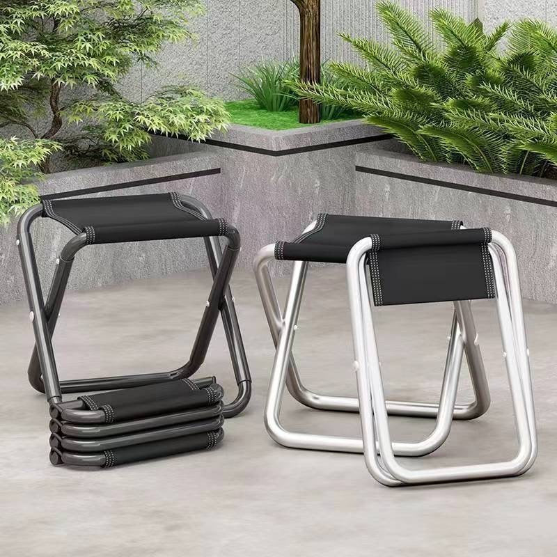 Two aluminum folding camp stools, black and silver, stacked on a stone patio outdoors