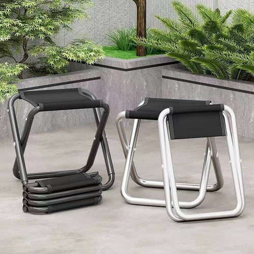 Two aluminum folding camp stools, black and silver, stacked on a stone patio outdoors
